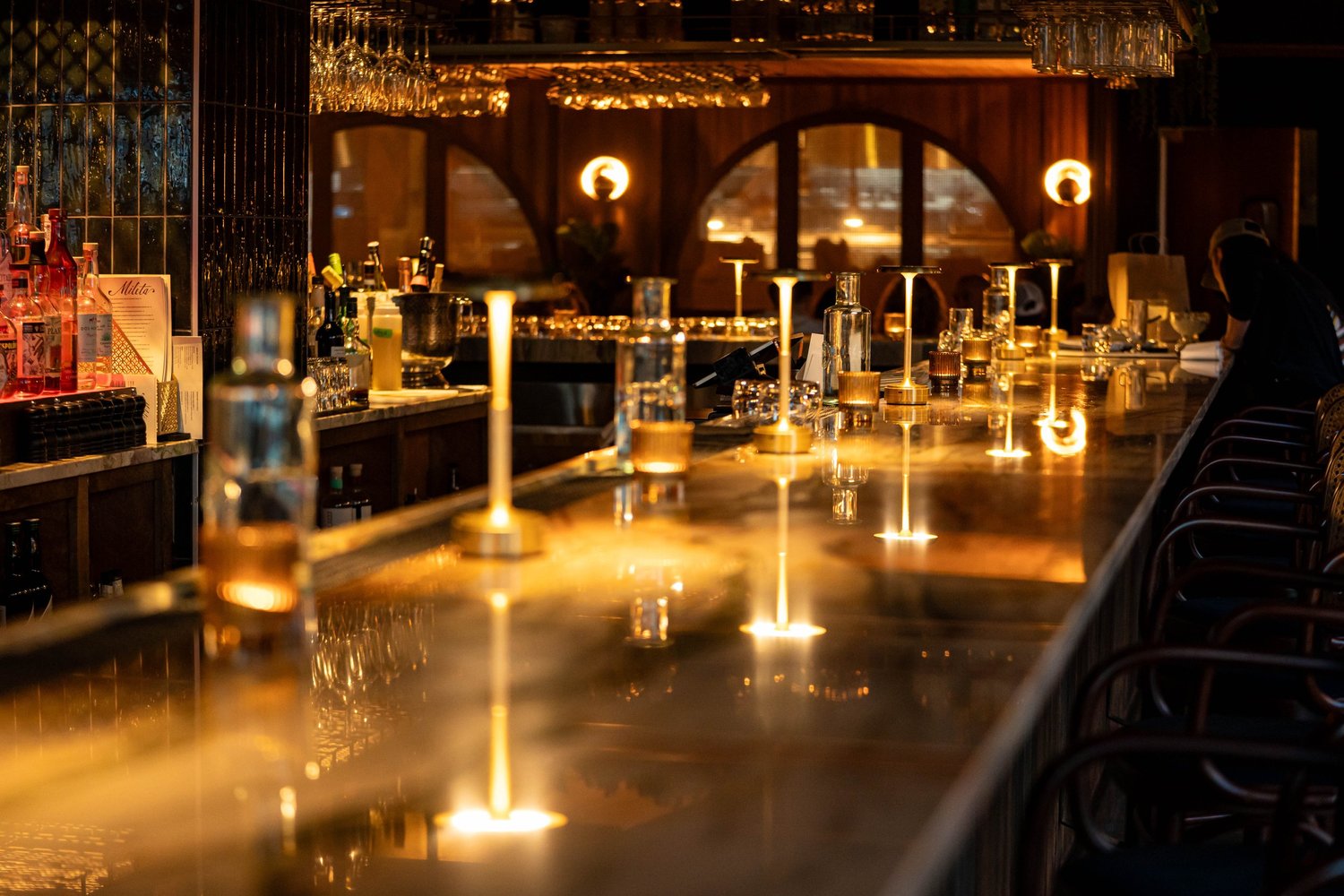 The long marble bar at Mileta at night, lit by small brass lamps